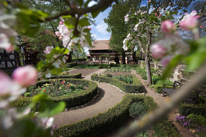 A garden with neatly trimmed hedges, flowering plants, and a traditional building with a tiled roof. 2