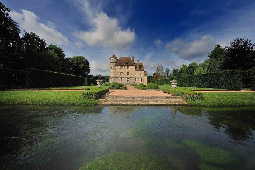A large stone castle with a moat in front, surrounded by well-manicured gardens and trees. 1