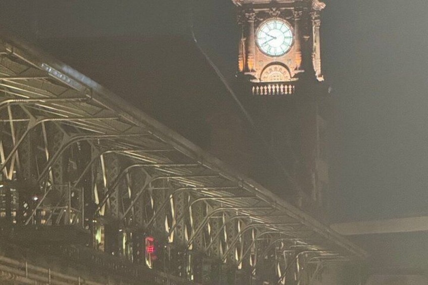 A clock tower with a clock face, a bridge with metal cables, and a cityscape in the background. 5