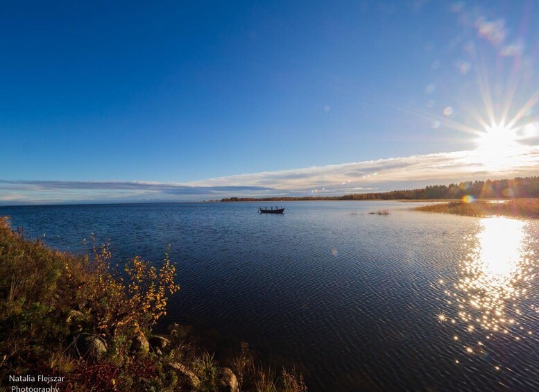 A calm lake with a boat in the distance, surrounded by trees and a clear sky. 1