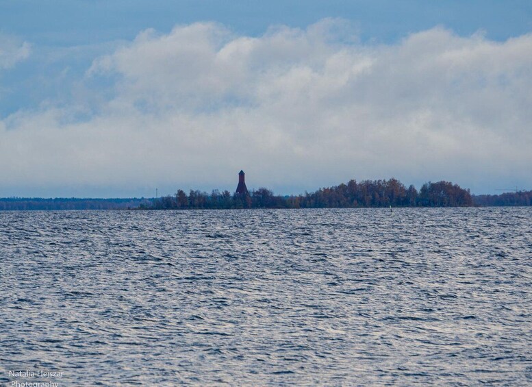 A lighthouse on a small island with a forested shoreline and a body of water. 3