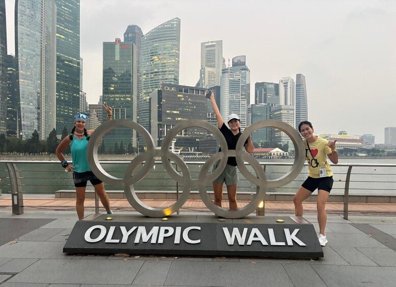 Three people posing with Olympic rings in front of a city skyline. 3