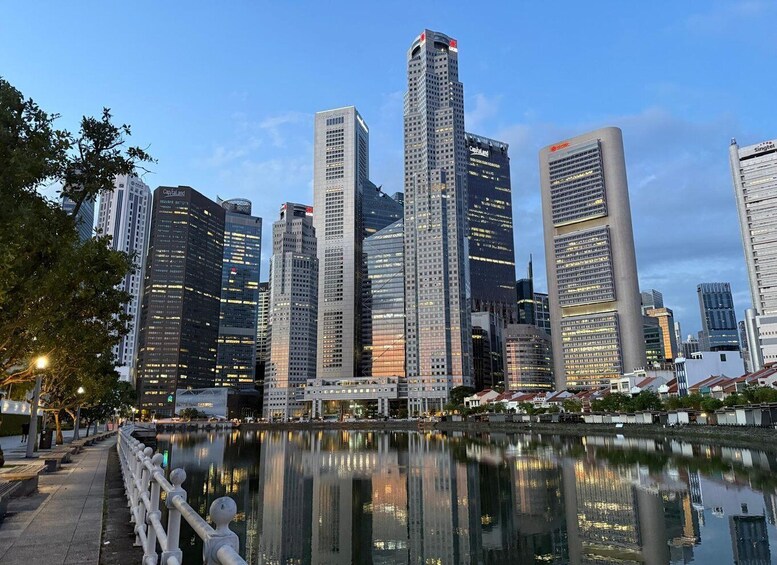 A city skyline with tall buildings, a body of water reflecting the structures, and a pedestrian walkway with a railing. 1