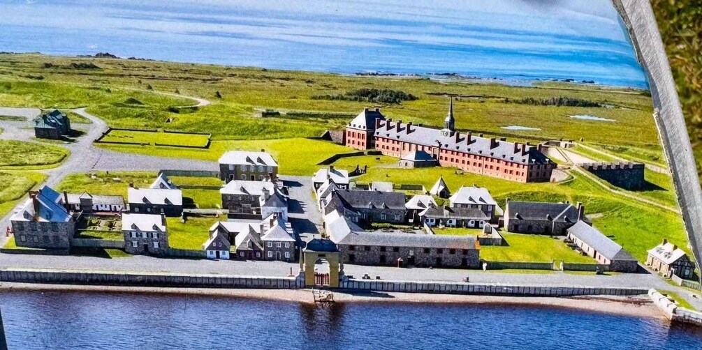 A coastal fort with a large red building, smaller stone structures, and a surrounding moat. 3