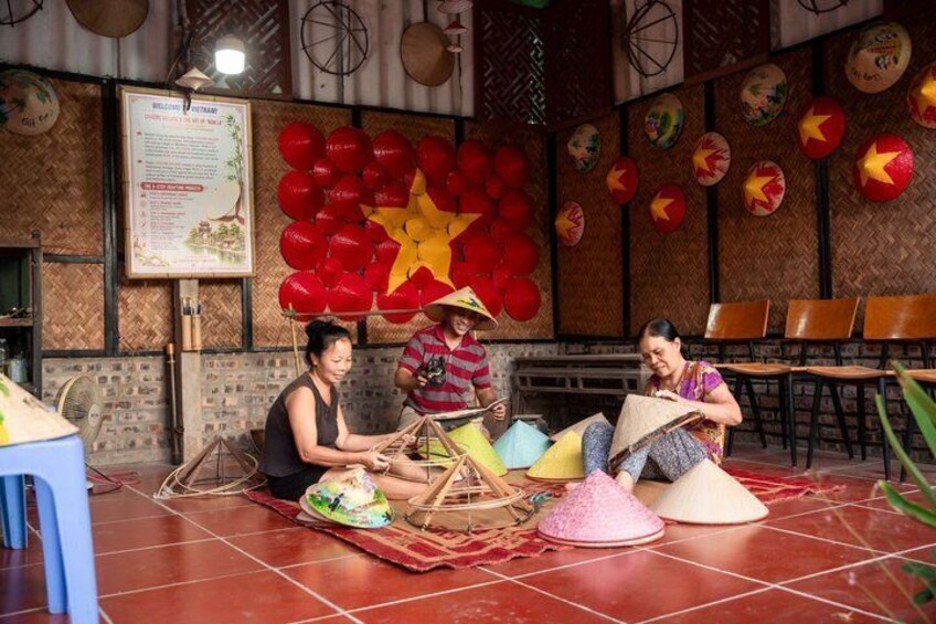 A group of people sitting on mats with traditional conical hats, a star decoration, and a menu board in a restaurant. 4
