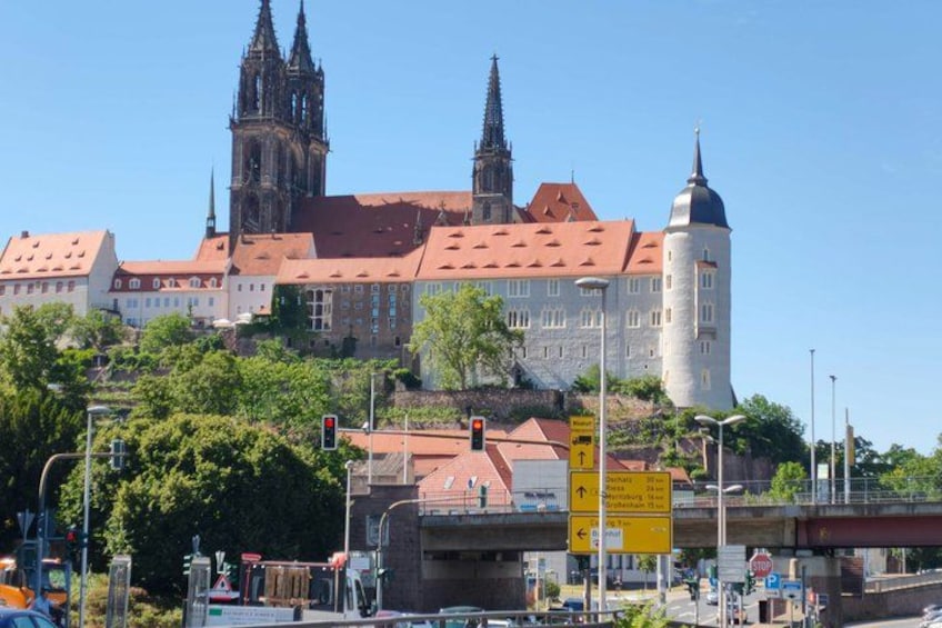 A historic building with a red roof, a tall tower, and a cathedral with spires in the background. 1