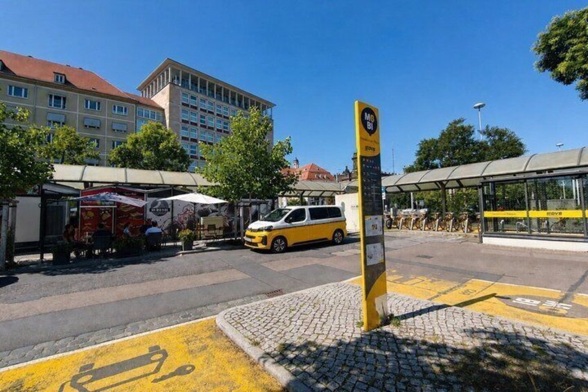 A bus stop with a shelter, a yellow bus, and a building in the background. 3