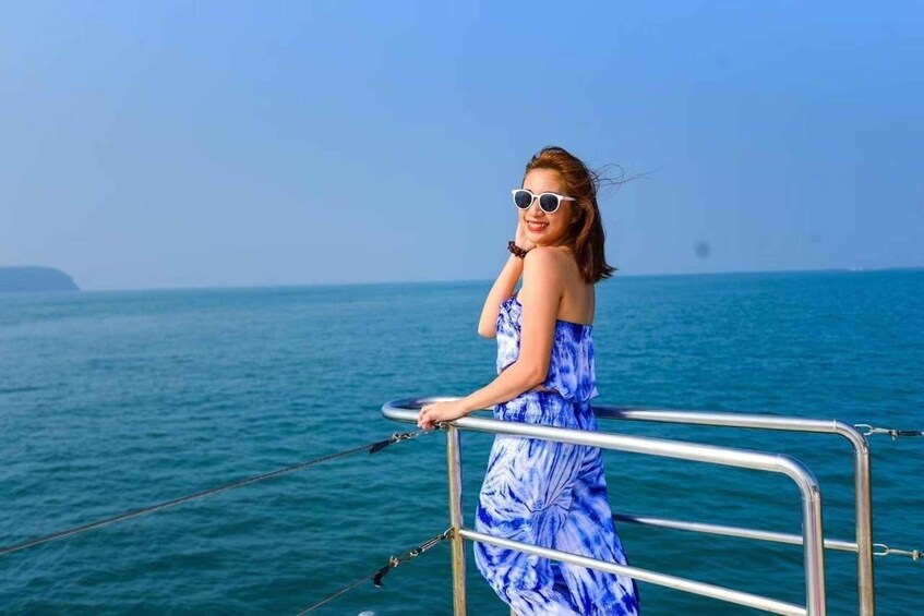A person in a blue dress standing on a boat, holding onto a railing, with a calm sea and a clear sky in the background. 3