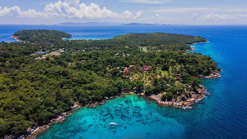 An aerial view of a coastal area with dense green vegetation, clear turquoise waters, and distant islands. 5