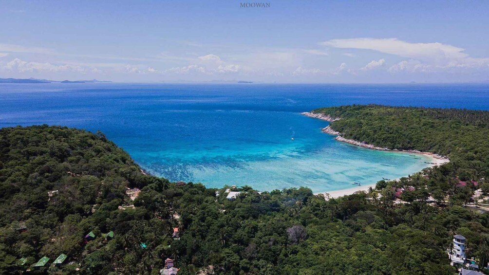 A coastal landscape with a clear blue sea, a sandy beach, and dense green vegetation. 4