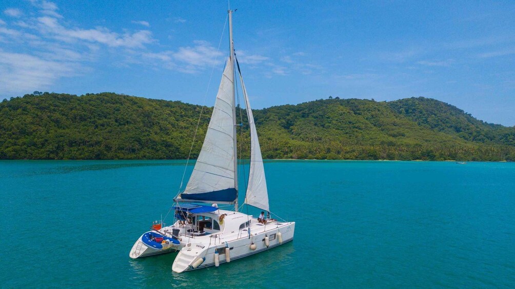A sailboat on turquoise water with a forested island in the background. 1