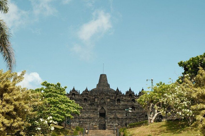 A stone temple with a pointed roof, surrounded by lush greenery and trees. 3
