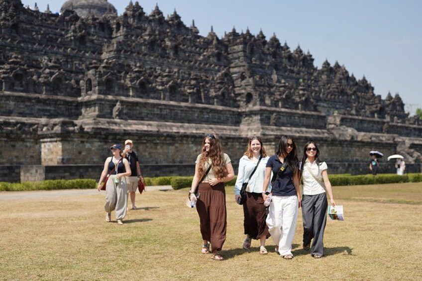 A group of people walking in front of a large, ancient stone structure with intricate carvings. 1