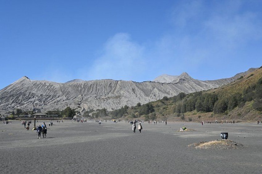 A volcanic landscape with a large crater, people walking, and a clear sky. 4