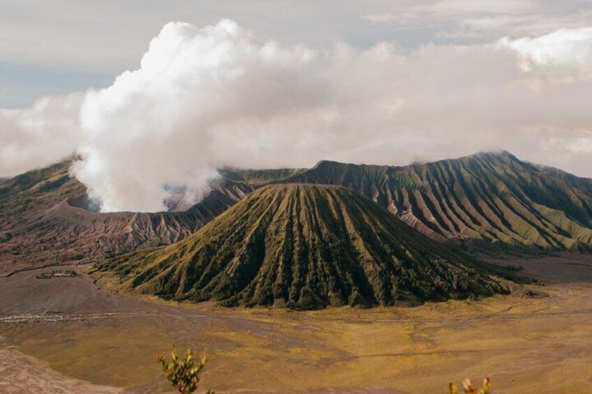 A volcanic landscape with a prominent crater emitting smoke, surrounded by rugged terrain. 5