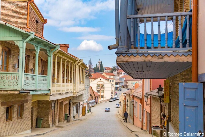 A narrow street lined with historic buildings, a man walking down the street, and a blue door on the right. 2