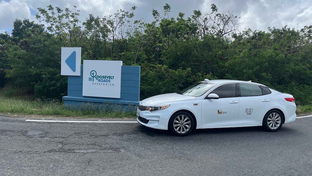 A white car parked in front of a sign for Roosvelt Roads in Puerto Rico. 1