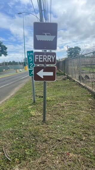 A ferry sign with a boat symbol and an arrow pointing left, next to a road with a green directional sign. 3