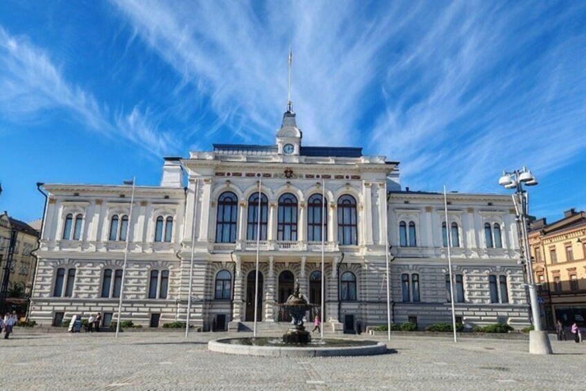 A large, historic building with a central entrance, a fountain in front, and a clear blue sky. 2