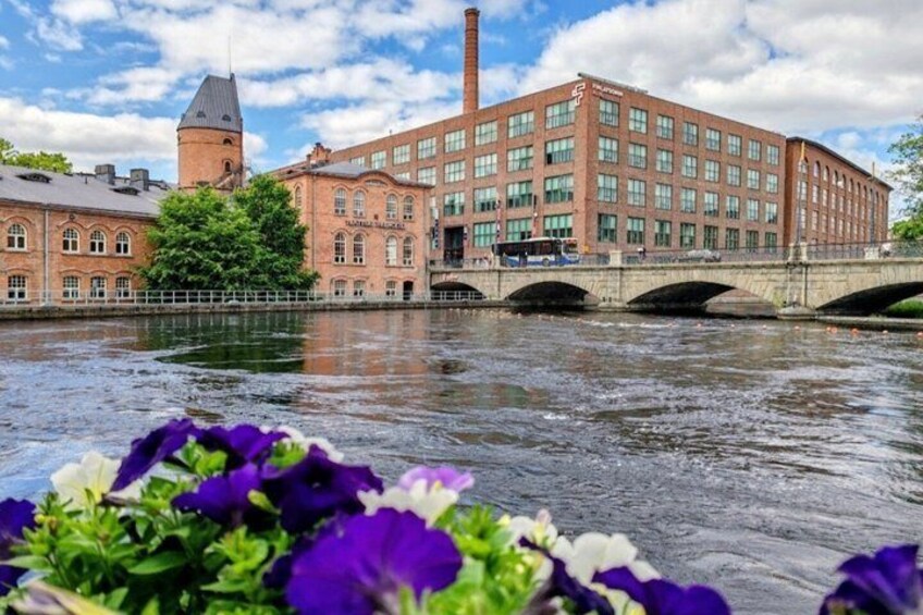 A river with a bridge, a brick building with a tower, and flowers in the foreground. 5