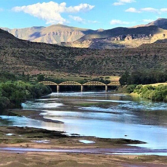 A river with a bridge, mountains, and greenery. 1