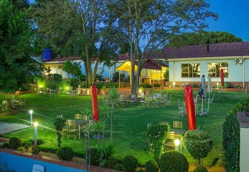 A well-lit outdoor area with tables and chairs, surrounded by greenery and trees. 5
