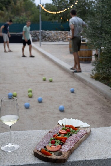 A bocce ball court with players, a wine glass, and a charcuterie board. 4