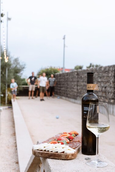 A bottle of wine and a glass on a concrete ledge with a wooden board of cheese and tomatoes in the foreground. 5