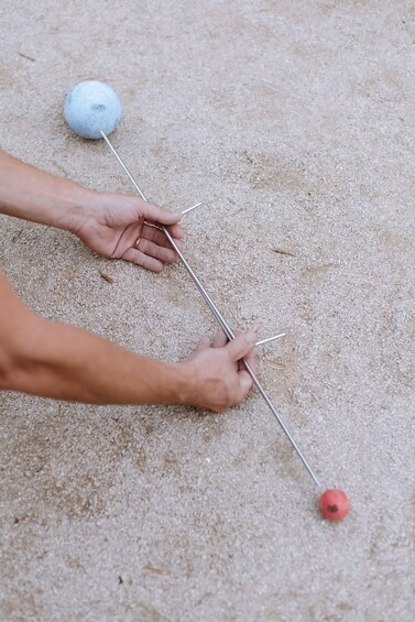 A person using a metal tool to dig into sandy ground. 3