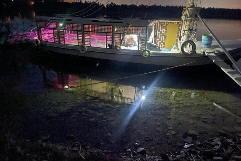 A boat with a cabin and a covered area, docked at night with lights reflecting on the water. 4