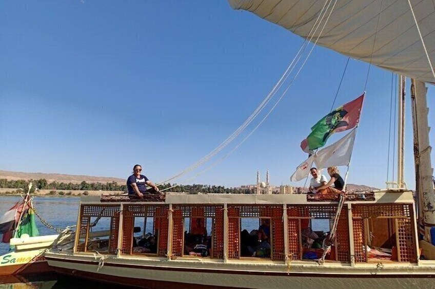 A boat with a flag, a person sitting on the deck, and another person standing. 1