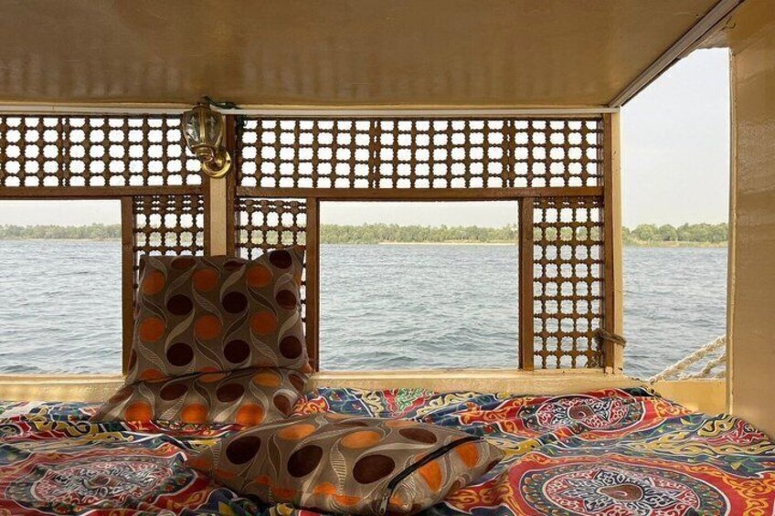 A boat interior with a patterned cushion, a lattice window, and a view of the water. 5