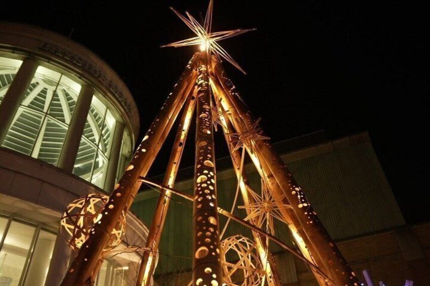 A tall, illuminated structure with a star at the top, possibly a decorative tower or monument, set against a building with large windows. 5