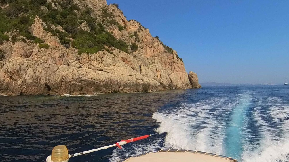 A boat moving through a body of water with a rocky coastline in the background. 3