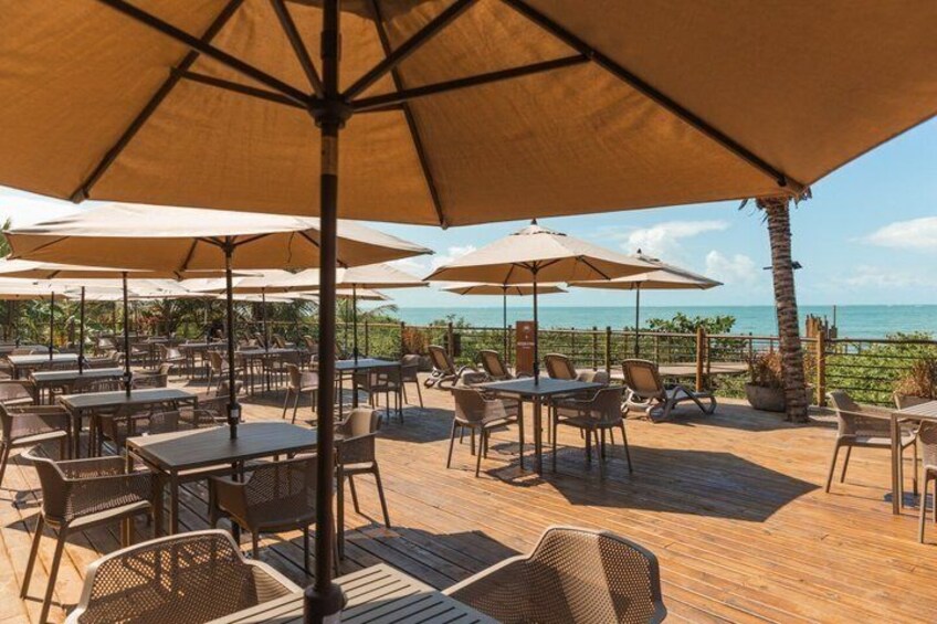 An outdoor patio with tables and chairs under large umbrellas, overlooking a beach. 1