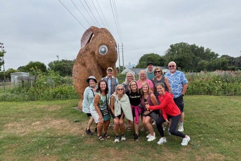 A group of people posing in front of a large sculpture of a fish. 3