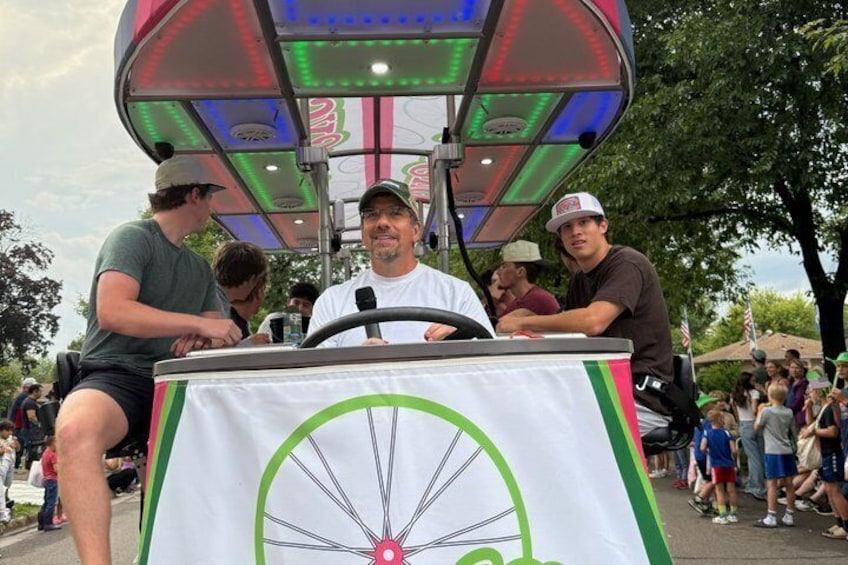 A man at a booth with a bicycle wheel design, people around, and a colorful canopy. 2