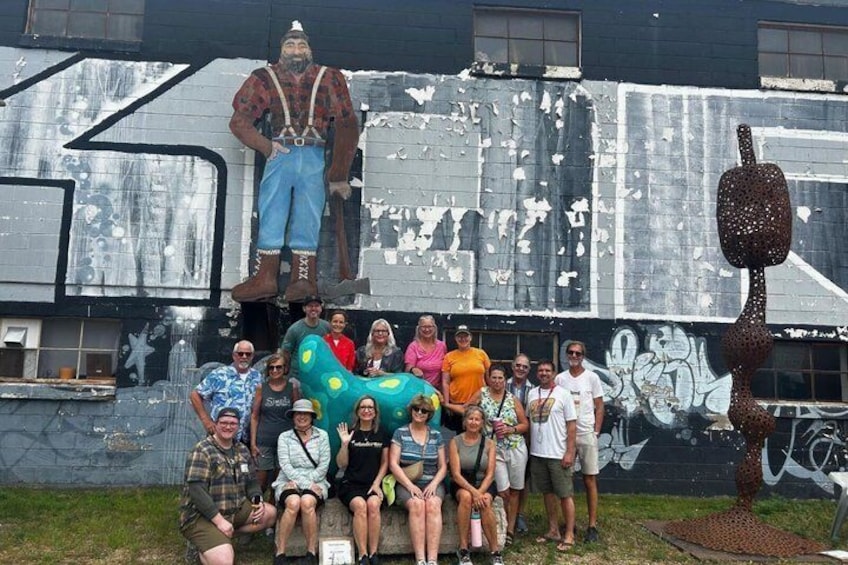 A group of people posing in front of a graffiti-covered wall with a large sculpture of a man and a colorful animal. 4