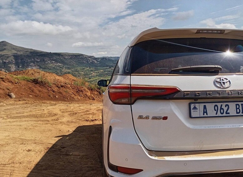A white Toyota Fortun G06 parked on a dirt road with a mountainous landscape in the background. 4