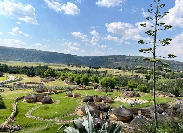 A rural landscape with traditional huts, a clear sky, and rolling hills in the background. 3