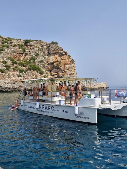 A boat named 'NIGARO' with people on board, docked near rocky cliffs. 3