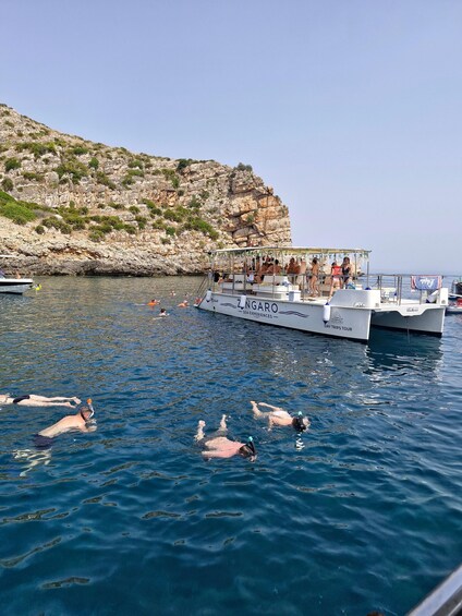 A boat named ZINGARO with people swimming in the water and a rocky cliff in the background. 2