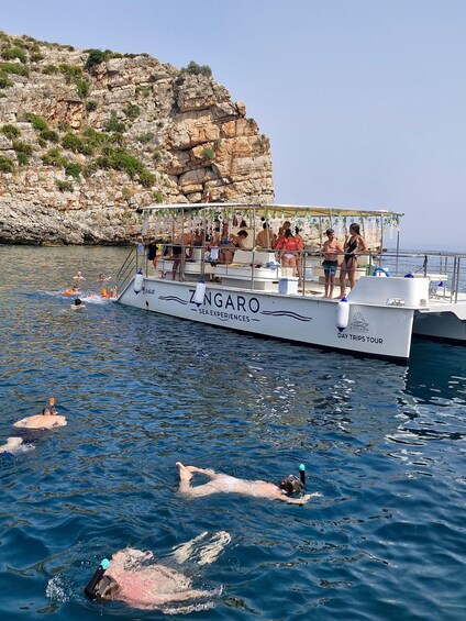 A boat named ZINGARO with people swimming and standing on it. 5