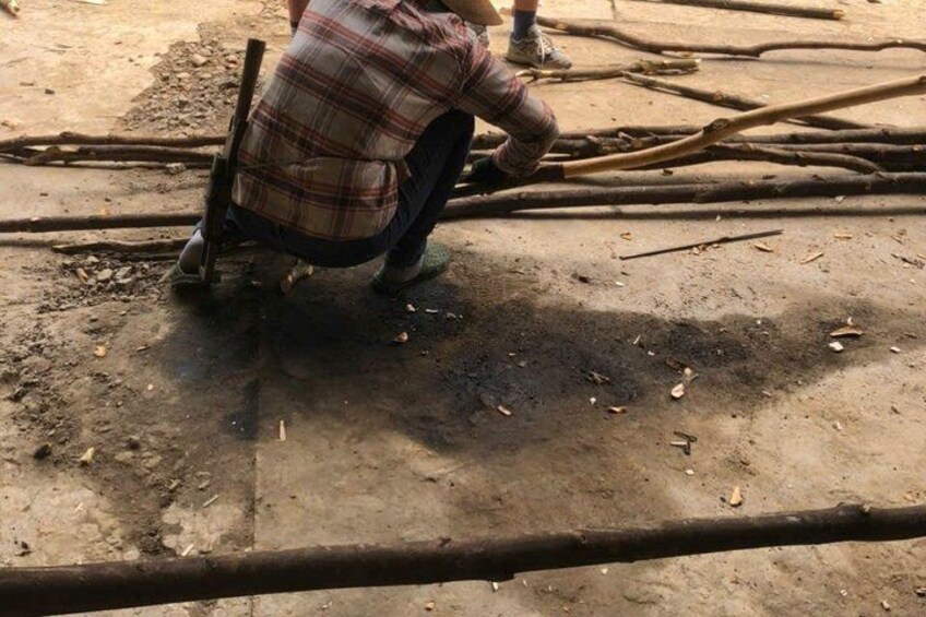A person crouching on a dirt ground with wooden planks and branches around. 3