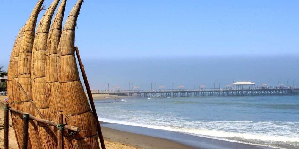 A beach with a wooden structure, ocean waves, a pier, and a distant building. 4