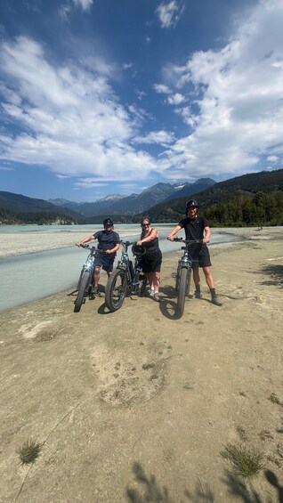 Three people on bicycles near a lake with mountains in the background. 3