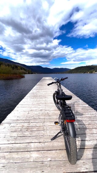 A mountain bike parked on a wooden dock extending into a lake with mountains in the background. 1
