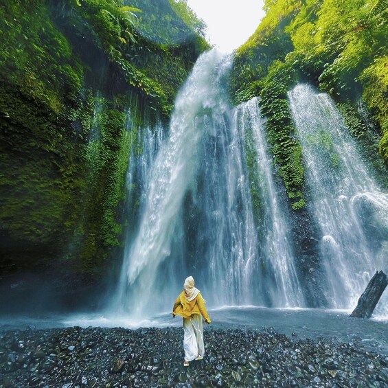 A waterfall with a person standing on a rocky foreground. 1