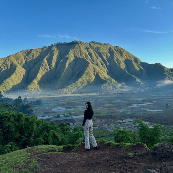 A person standing on a hill overlooking a valley with terraced fields and a mountain in the background. 2