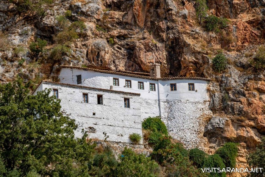 A white building with a tiled roof nestled in a rocky cliff. 1